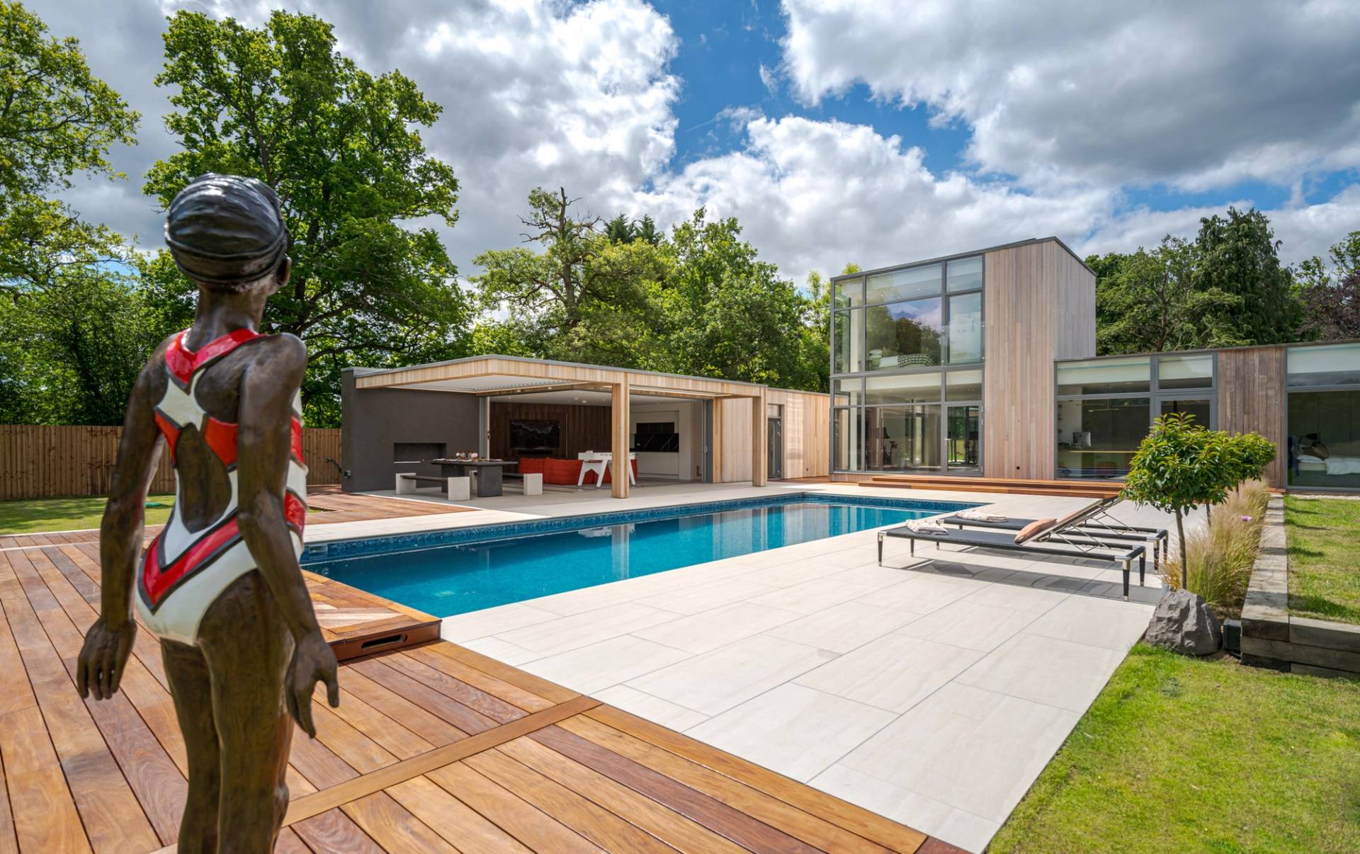 Love Locations ultra-modern house shoot location Godalming: Sunlit swimming pool wrapped in premium wooden decking and flat green lawns, optimized for swimwear campaigns and cinematic film.