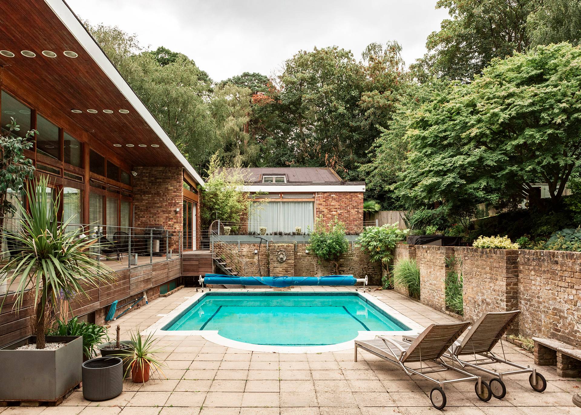 Mid-century modern architectural rear view highlighting the swimming pool terrace, sun loungers, and lush surrounding trees in Bromley, Love Locations.