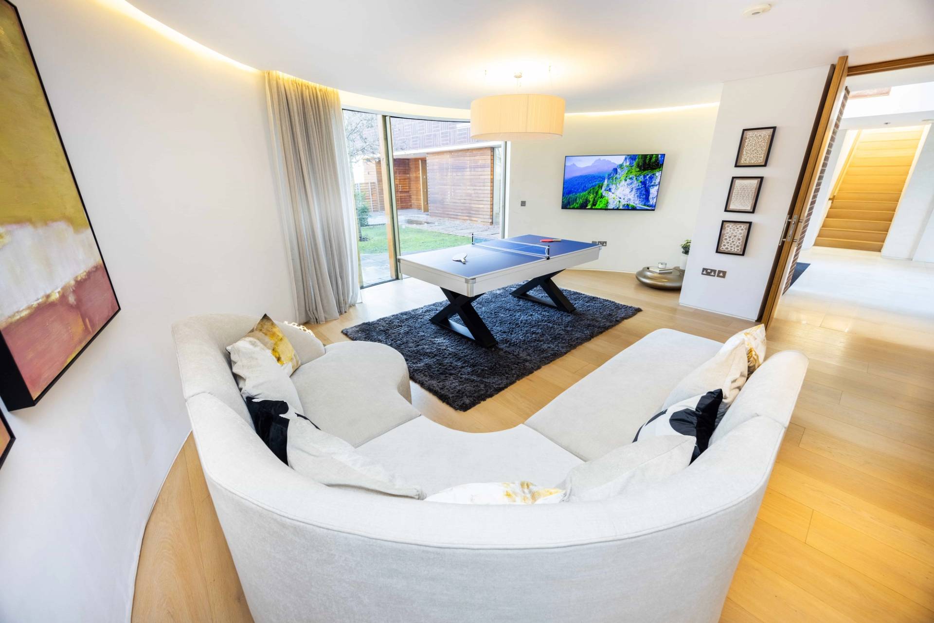 Games room suite in Radlett, WD7 featuring a white pool table, curved white sofa, and garden views, Love Locations.