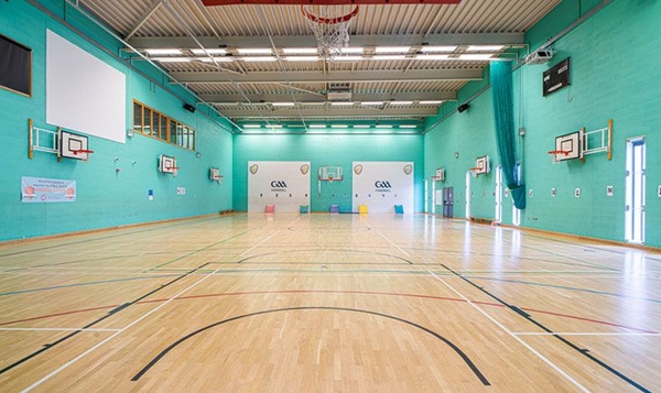 Love Locations school sports hall Reading South East London SE2: Large indoor gymnasium featuring teal panelled walls, basketball hoops, and crisp court markings, perfect for high-energy sports ads.