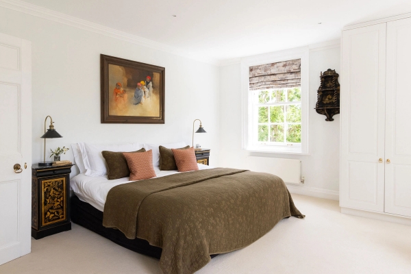 Love Locations neutral country house bedroom BN44: Guest room layout with an olive green throw blanket, terracotta cushions, and classic landscape oil paintings, excellent for domestic film scenes.