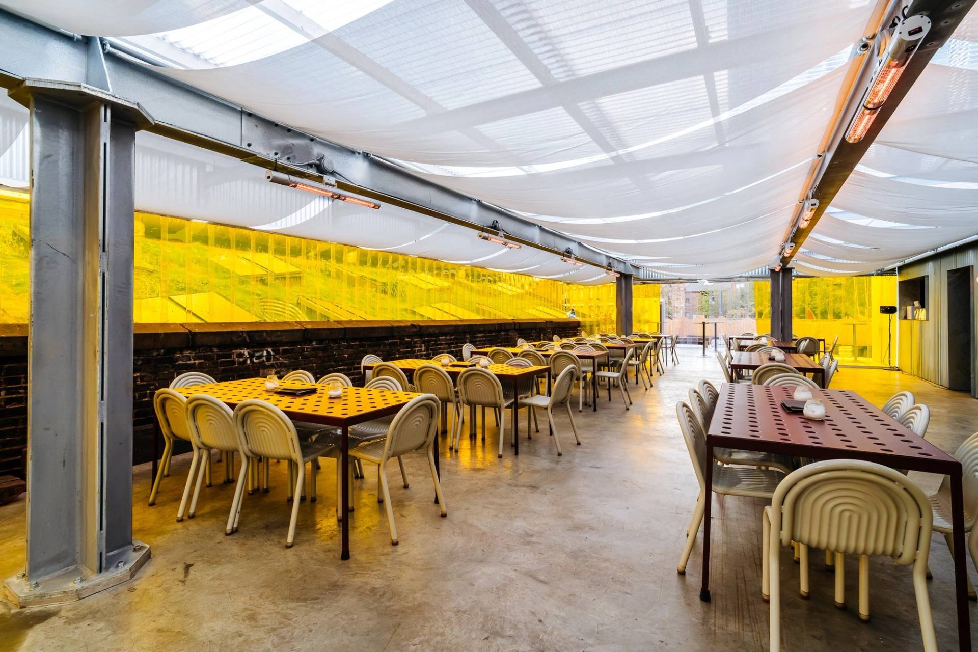 Sheltered outdoor bar and event terrace with warm overhead canopy lighting and yellow accent tables through Love Locations.