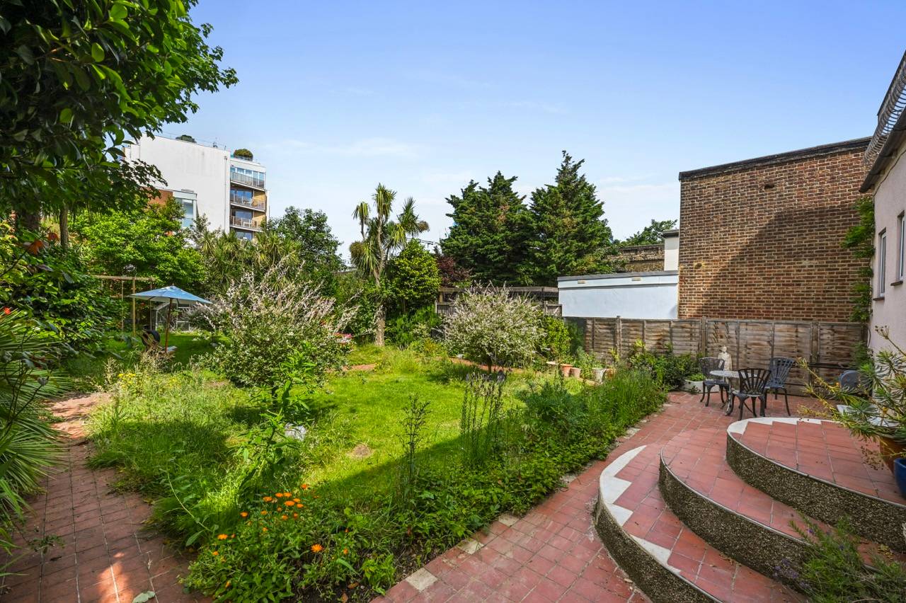 Manicured green lawn with curved brick patio steps and lush perimeter trees, Love Locations.