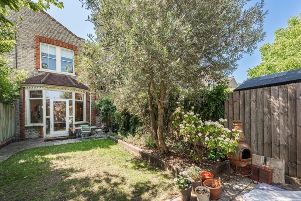 Secluded sunlit rear garden location with a lush green lawn and mature olive trees in Barnet, N11 via Love Locations.