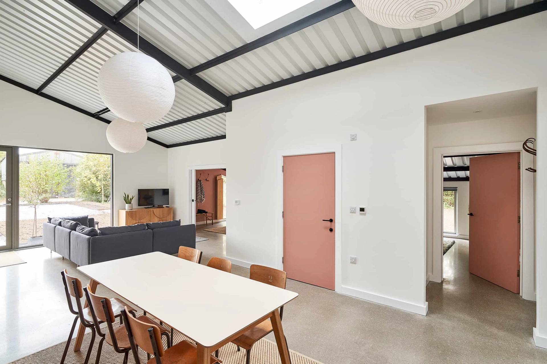 Bright open-plan dining room set under an industrial metal ceiling with a long wooden dining table and terracotta door accent, Love Locations IP30.