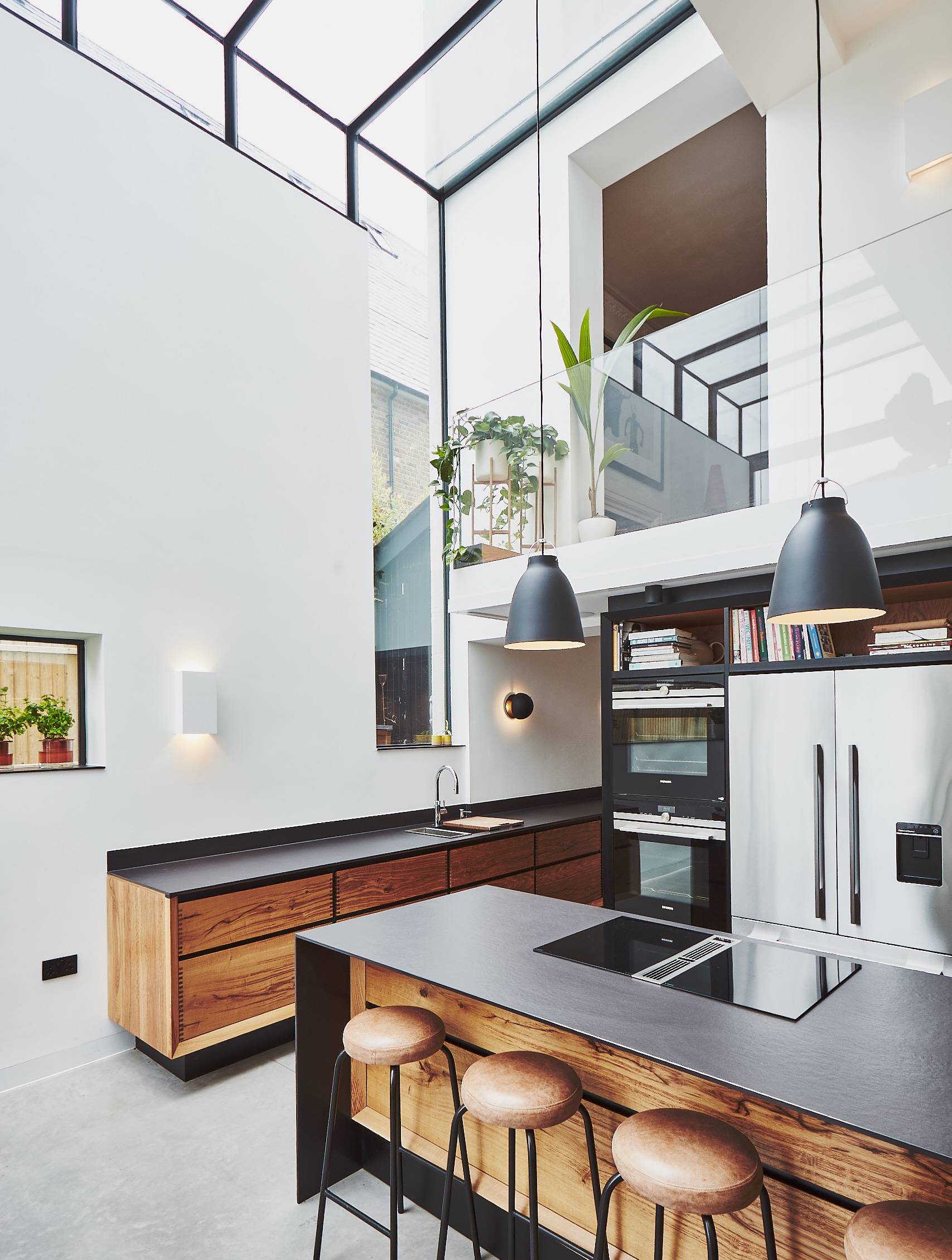 Contemporary open-plan kitchen view looking towards dark worktops, wooden cabinets, and double-height skylight void, Love Locations TW1.