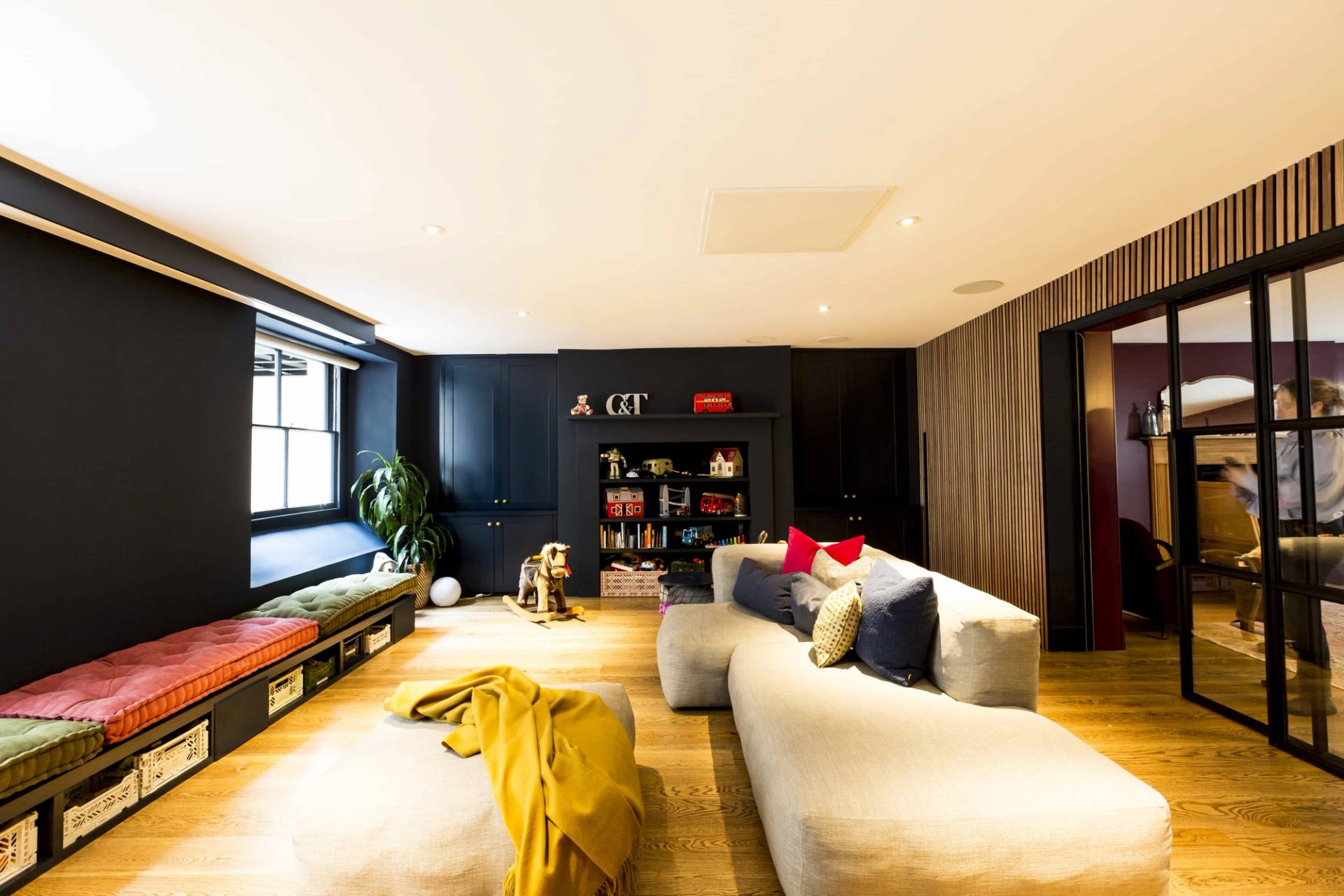 Cozy basement lounge location in Camberwell, SE5 featuring dark walls, grey sectional sofa, and colorful cushions via Love Locations.