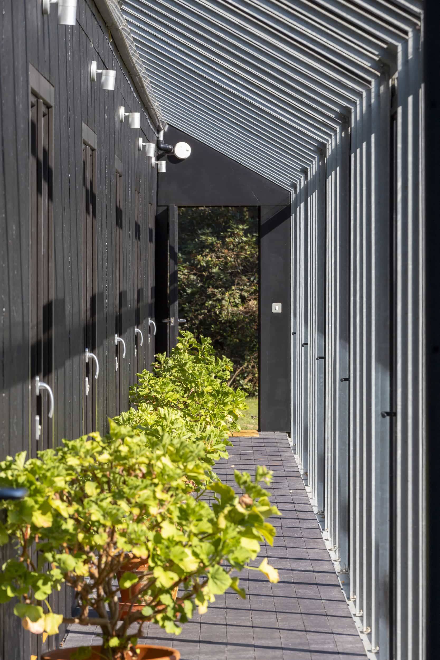 Modern black timber walkway corridor with glass roof section and lush green shrubbery, Love Locations IP17.