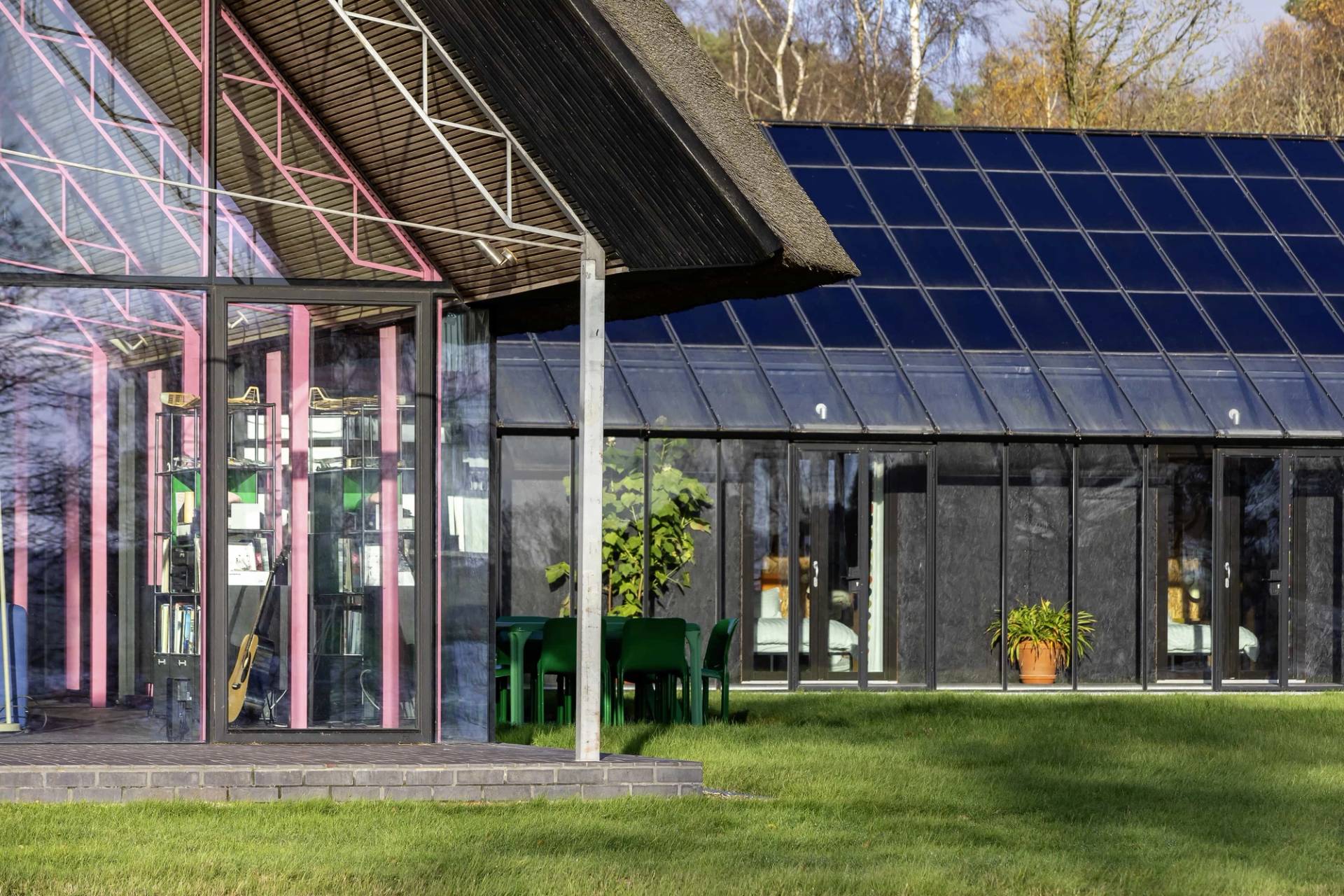 Modern thatched longhouse exterior with pink steel frame details set beside a solar panelled outbuilding, Love Locations IP17.