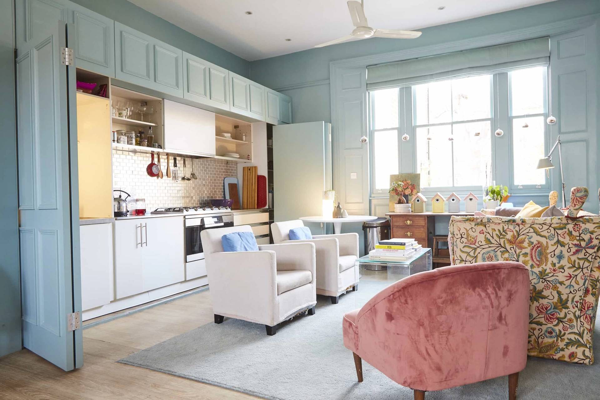 Duck-egg blue library room featuring built-in white kitchen cabinets, open bookshelves, and white armchairs, Love Locations N5.