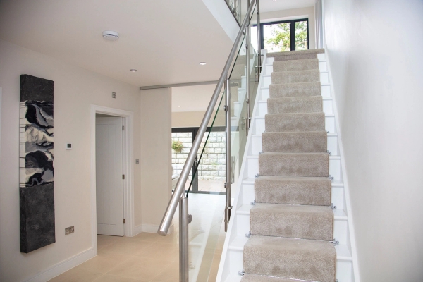 Grand contemporary staircase location house with a glass balustrade and plush beige carpeted steps for high-end corporate film sets, Love Locations.