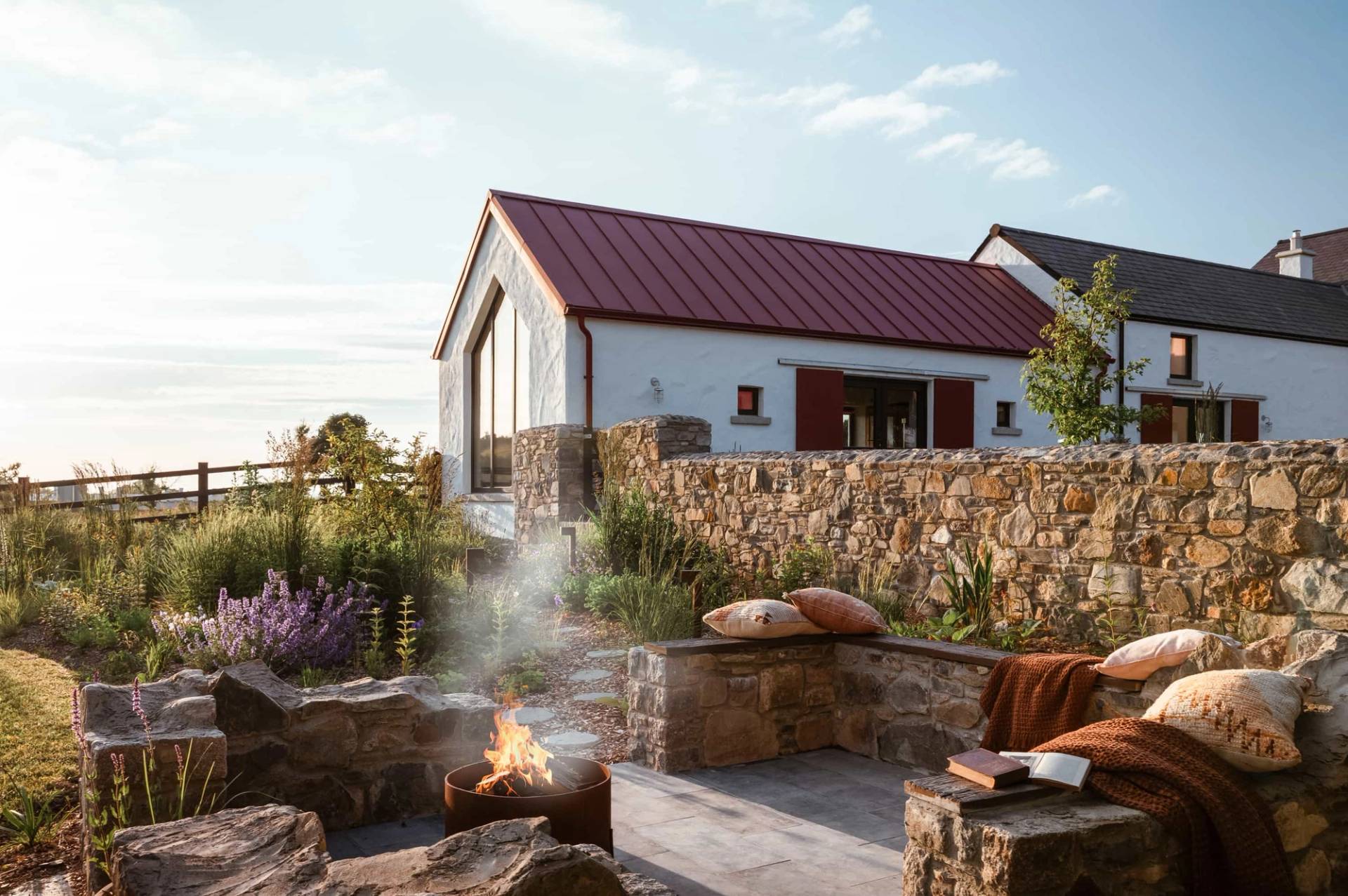 Sunken outdoor fire pit patio location in Castleblayney County Monaghan Ireland via Love Locations, set against a white farmhouse wing with a red tin roof.