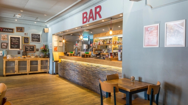 Sprawling timber bar counter and stone tile front with glowing red 'BAR' signage inside The Ritzy Cafe film location in Brixton SW2, available for production hire via Love Locations.