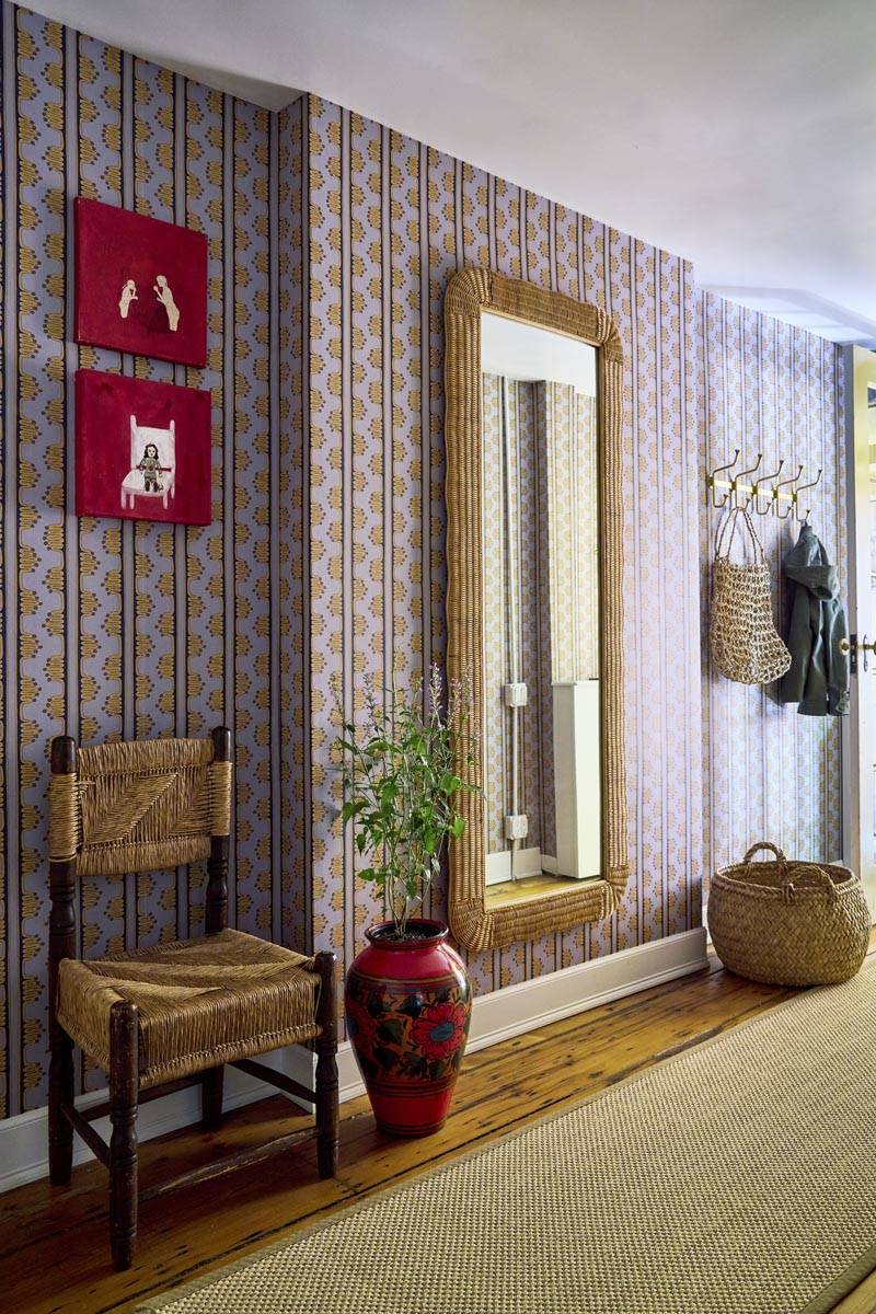 Stylish hallway entry shoot space with graphic patterned wallpaper, a tall wicker-framed mirror, and woven armchair in Manhattan NY 10014 through Love Locations.