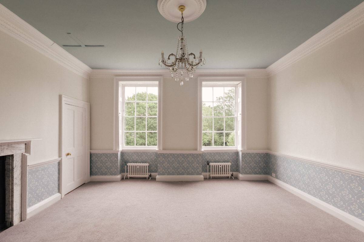 Neutral bedroom suite with blue patterned lower wall wallpaper, twin sash windows, and chandelier lighting, ideal for bedding lookbooks, Love Locations.