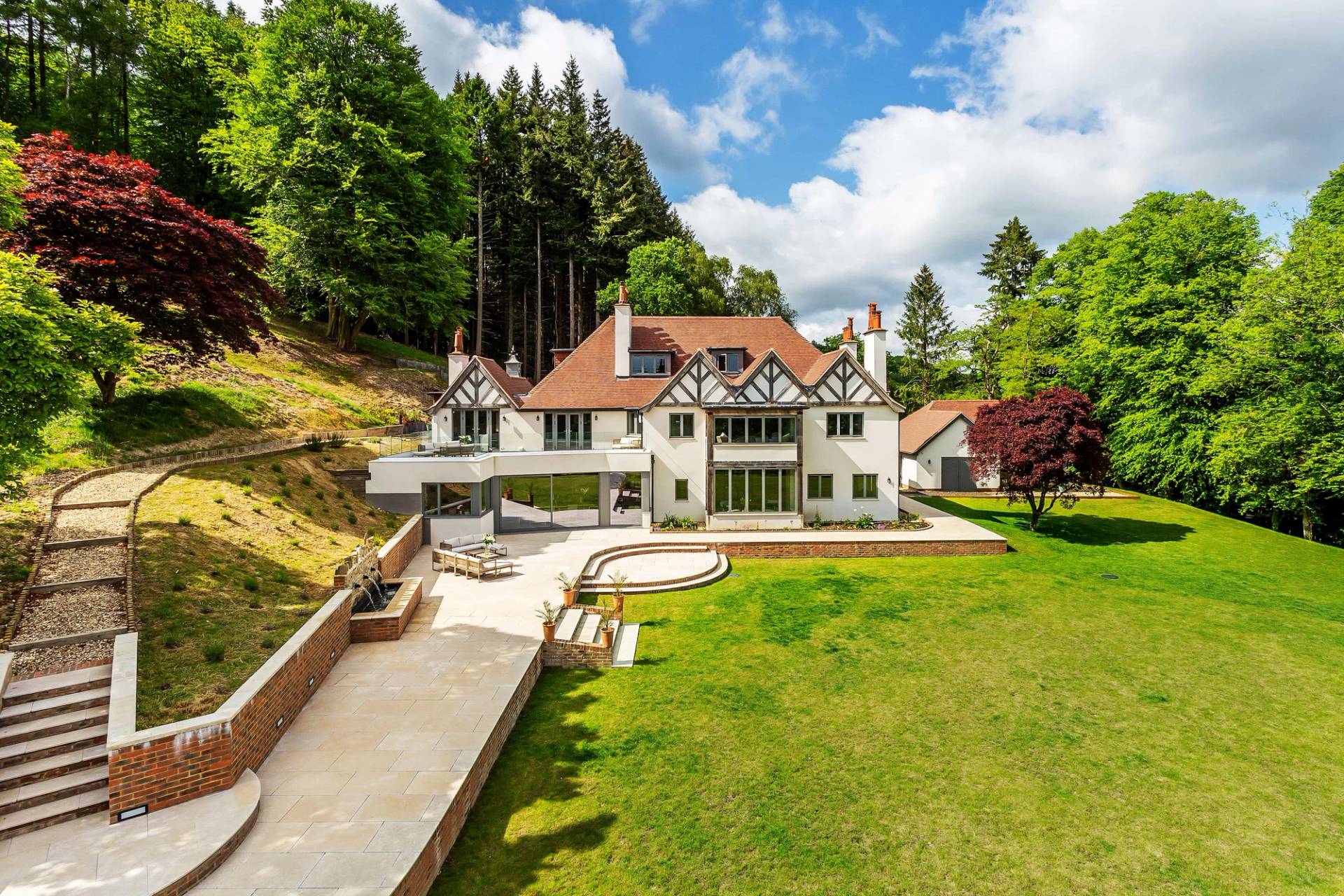 High-angle exterior view of a grand Surrey country house set amongst manicured lawns and mature forest, ideal for feature film establishing shots, Love Locations GU27.