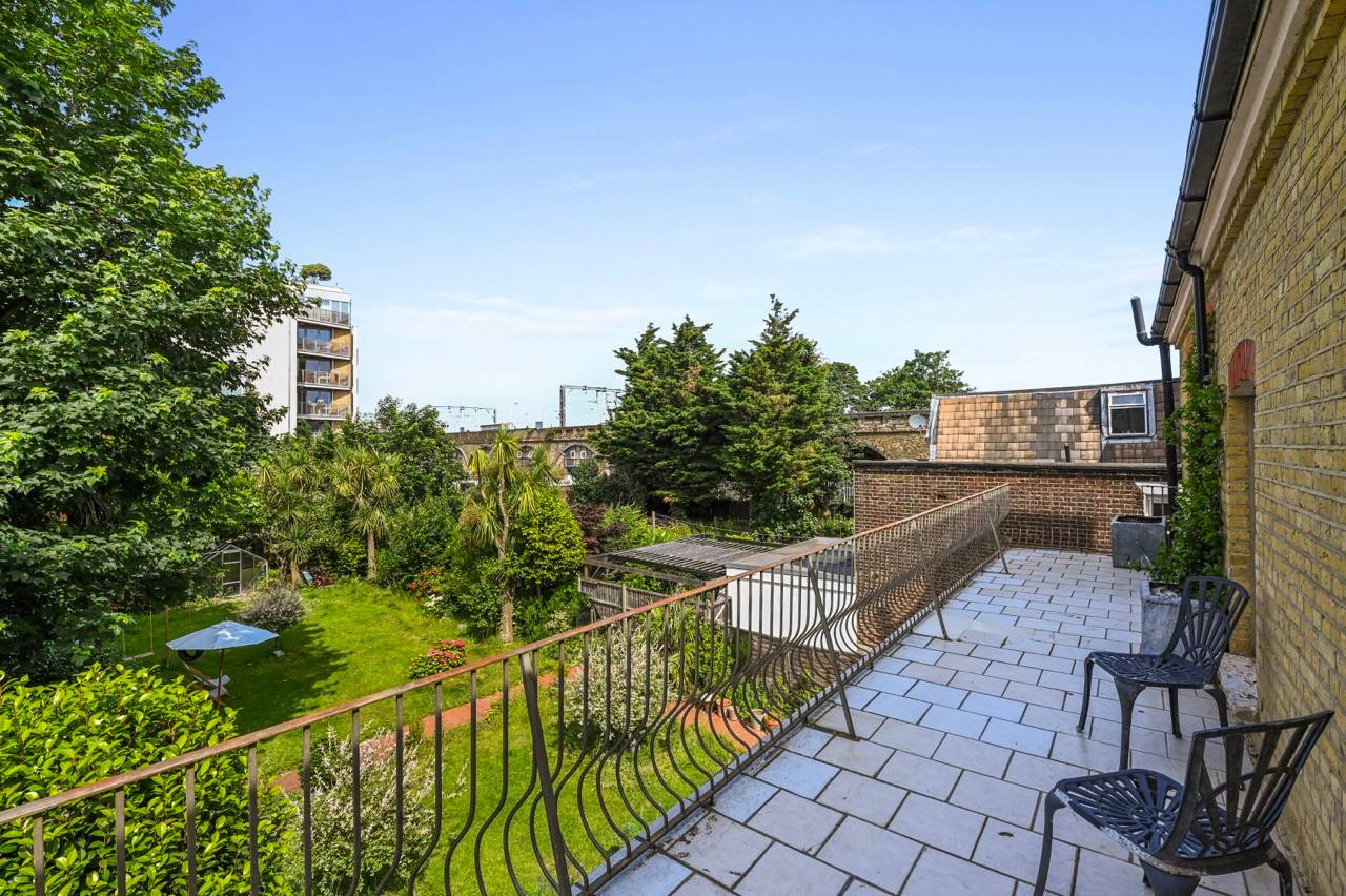 First-floor outdoor sun terrace featuring wrought-iron railings and green garden views in Newham, Love Locations E7.