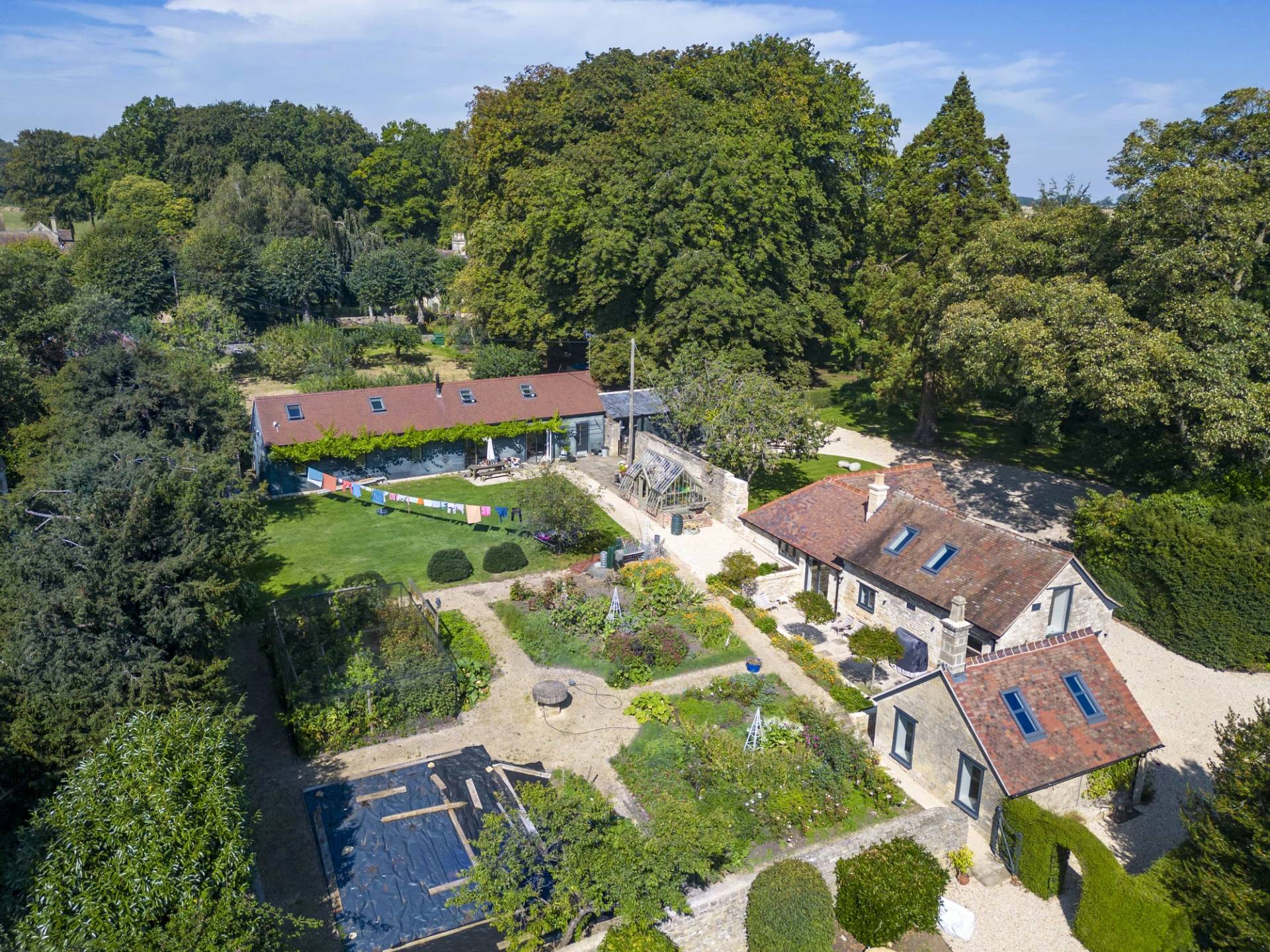 Aerial drone perspective of a historic manor house estate surrounded by lush gardens and outbuildings, Love Locations OX7.