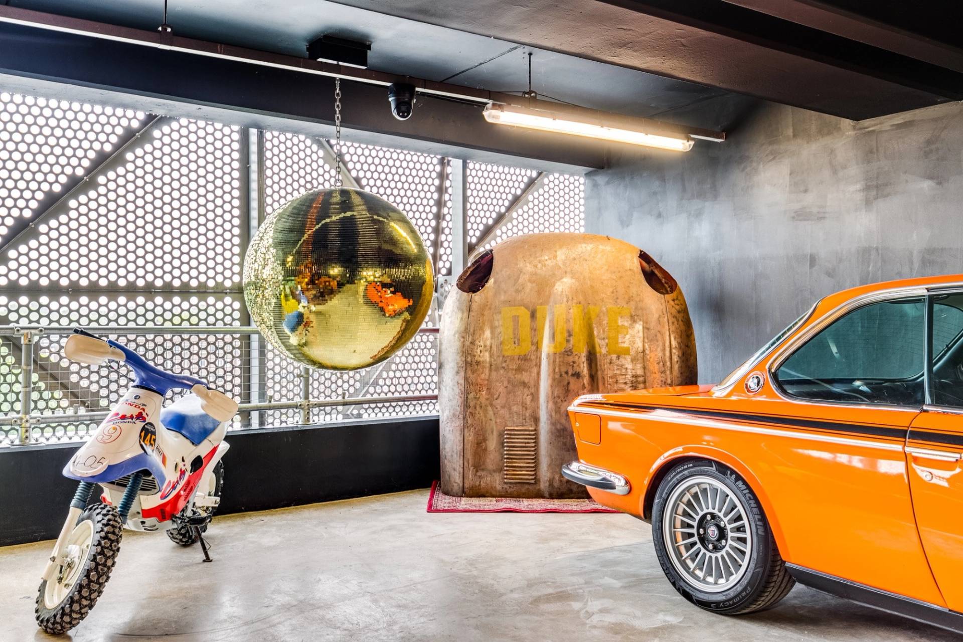 Industrial car storage showroom with gold disco ball and vintage orange car in Brentford TW8 through Love Locations.