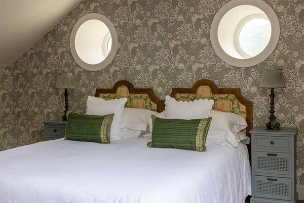 Glenstriven attic twin-bed room with porthole windows and decorative floral wallpaper in country estate setting.