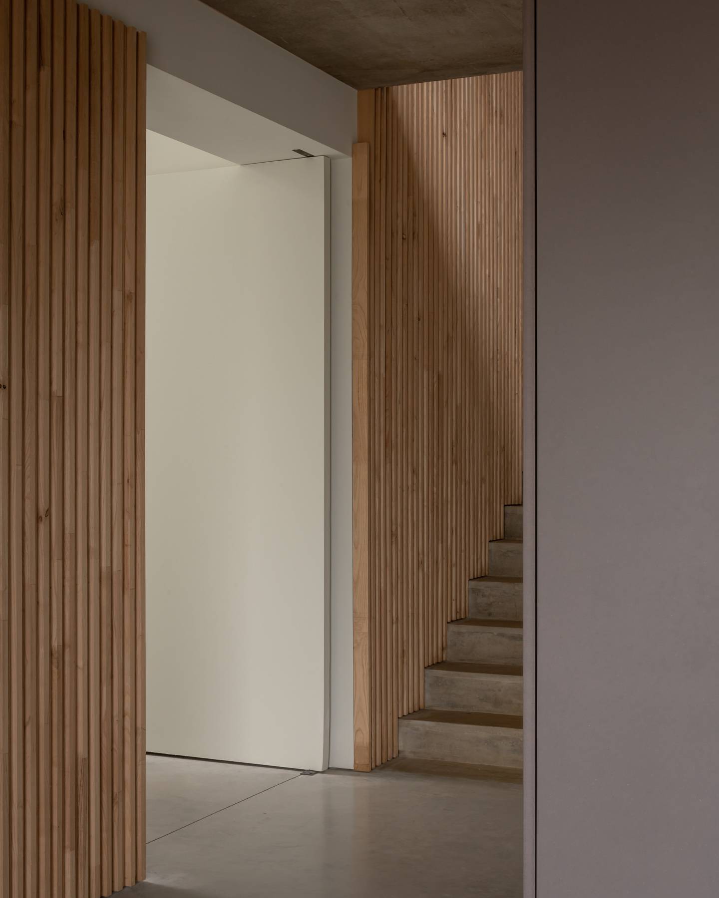 Bespoke vertical oak slat wall detail framing a doorway with concrete staircase treads, Love Locations BN3.