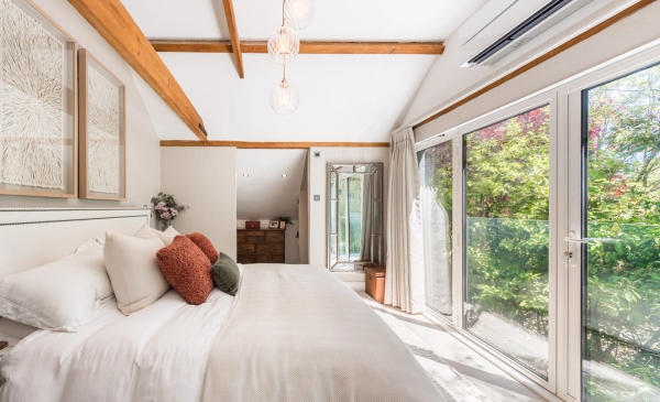 Minimalist barn conversion bedroom with extensive white fitted wardrobes and scenic country views, through Love Locations.