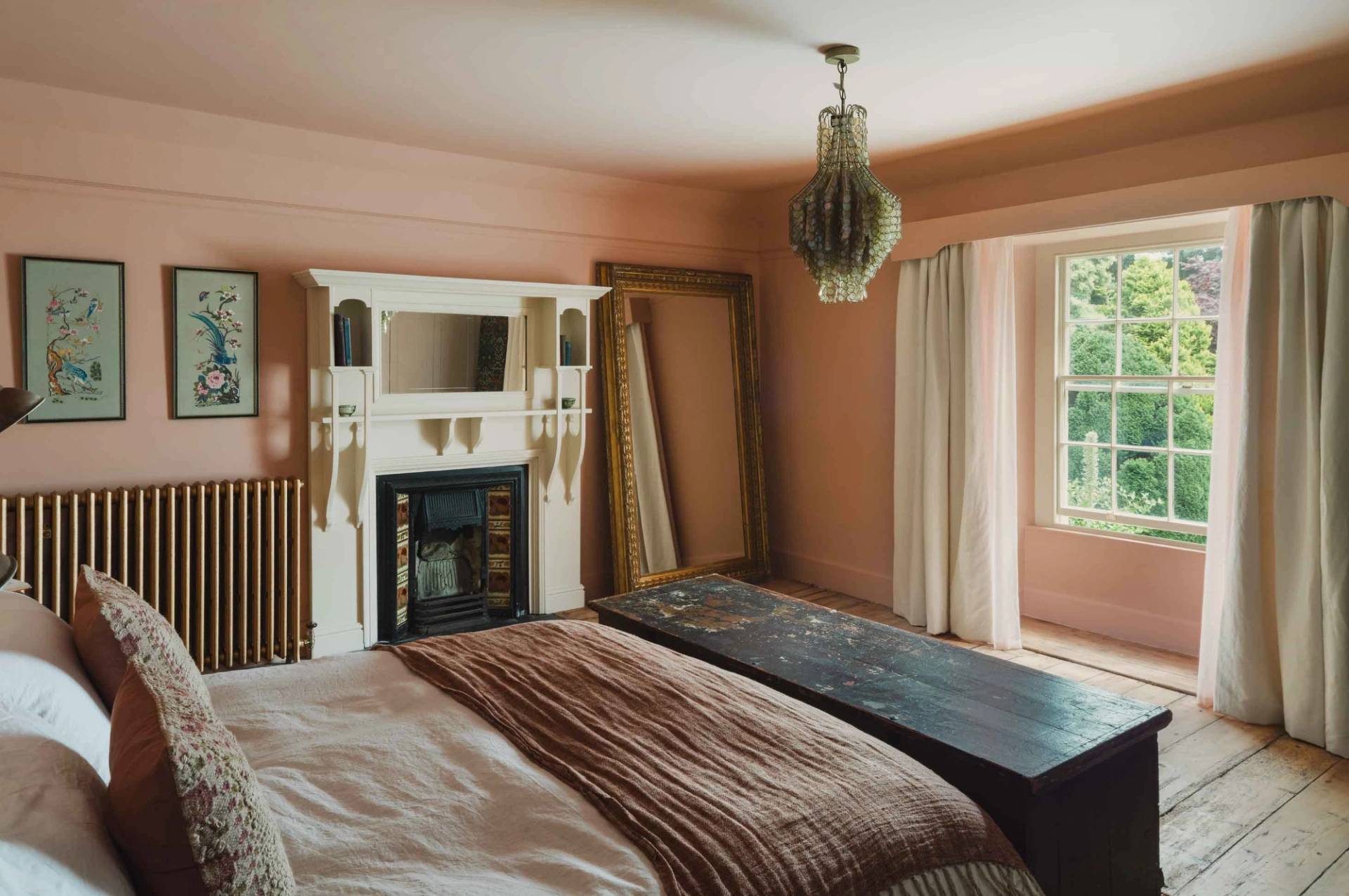 Spacious pink bedroom suite with a period fireplace mantel and glass light pendant in Newquay Cornwall TR8 by Love Locations.