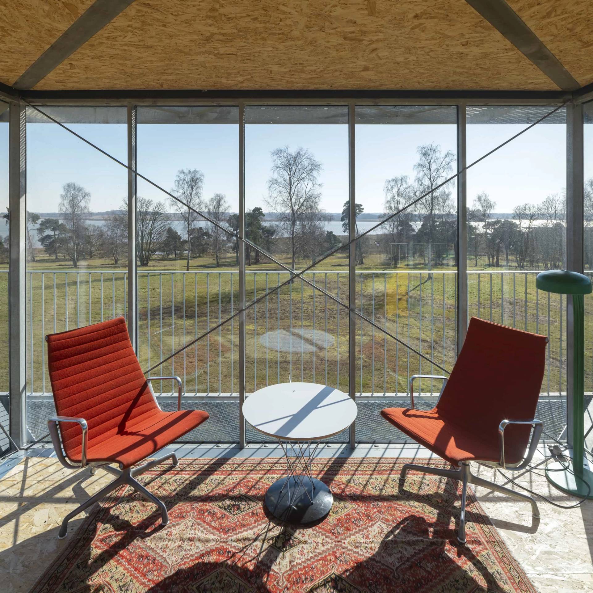 Interior view of an elevated glass lookout room with red armchairs, rug, and panoramic views of Suffolk countryside, Love Locations IP17.