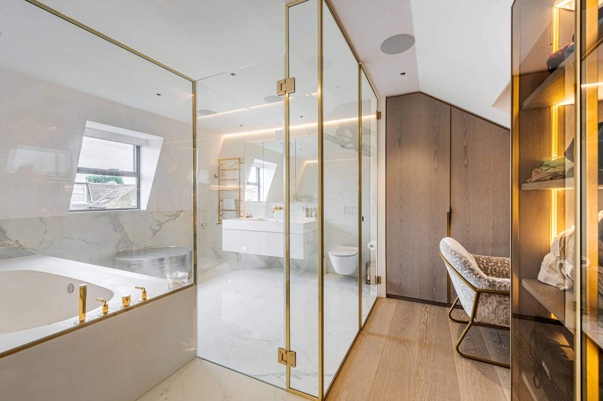 Ensuite bathroom with gold brass framed shower enclosure, vanity unit, and neutral marble finish, Love Locations SW11.