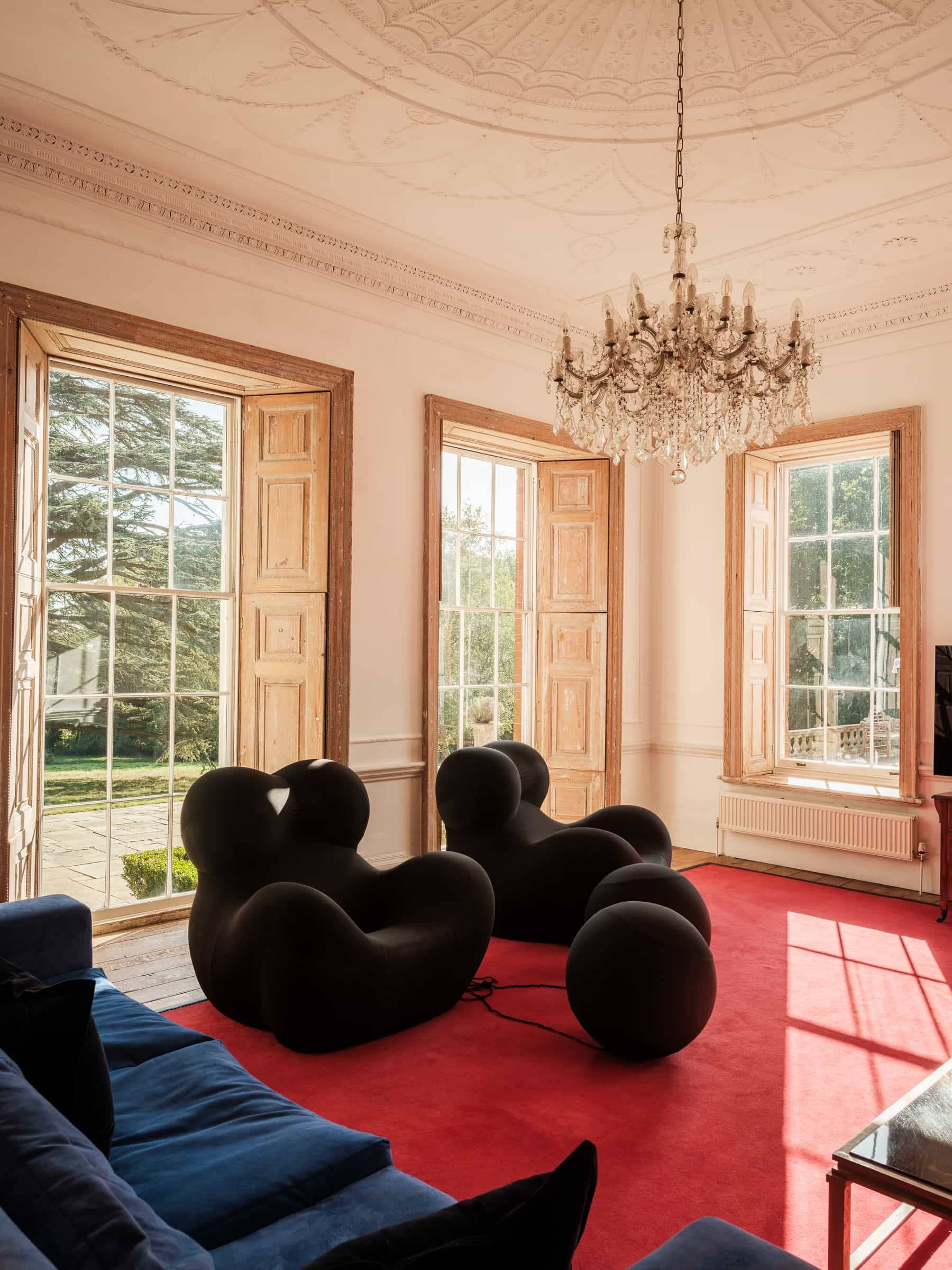 Grand sitting room featuring red carpets, black leather armchairs, ornate ceiling coving, and shuttered windows, Love Locations RG42.