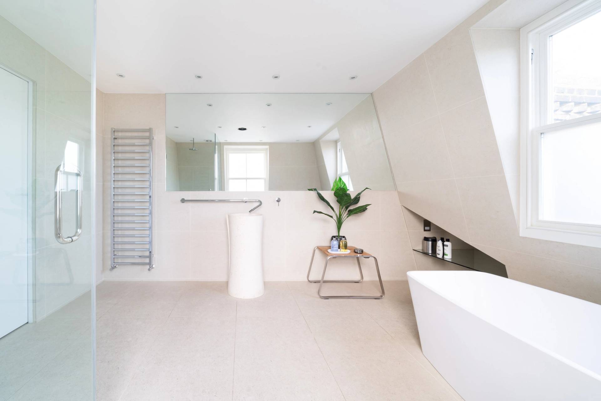 Minimalist attic bathroom with a freestanding bathtub, pedestal sink, and skylight window illumination, Love Locations SW6.