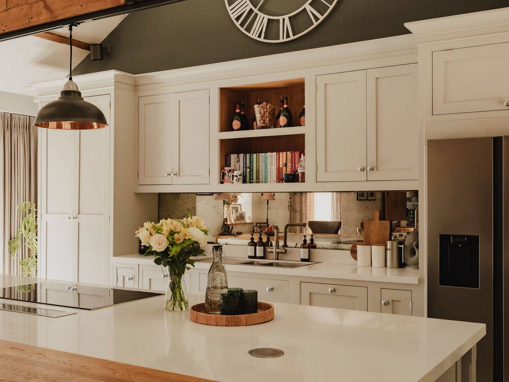 Sleek kitchen island counter with fresh flowers and mirror splashback detail inside a luxury rural barn conversion, Love Locations.