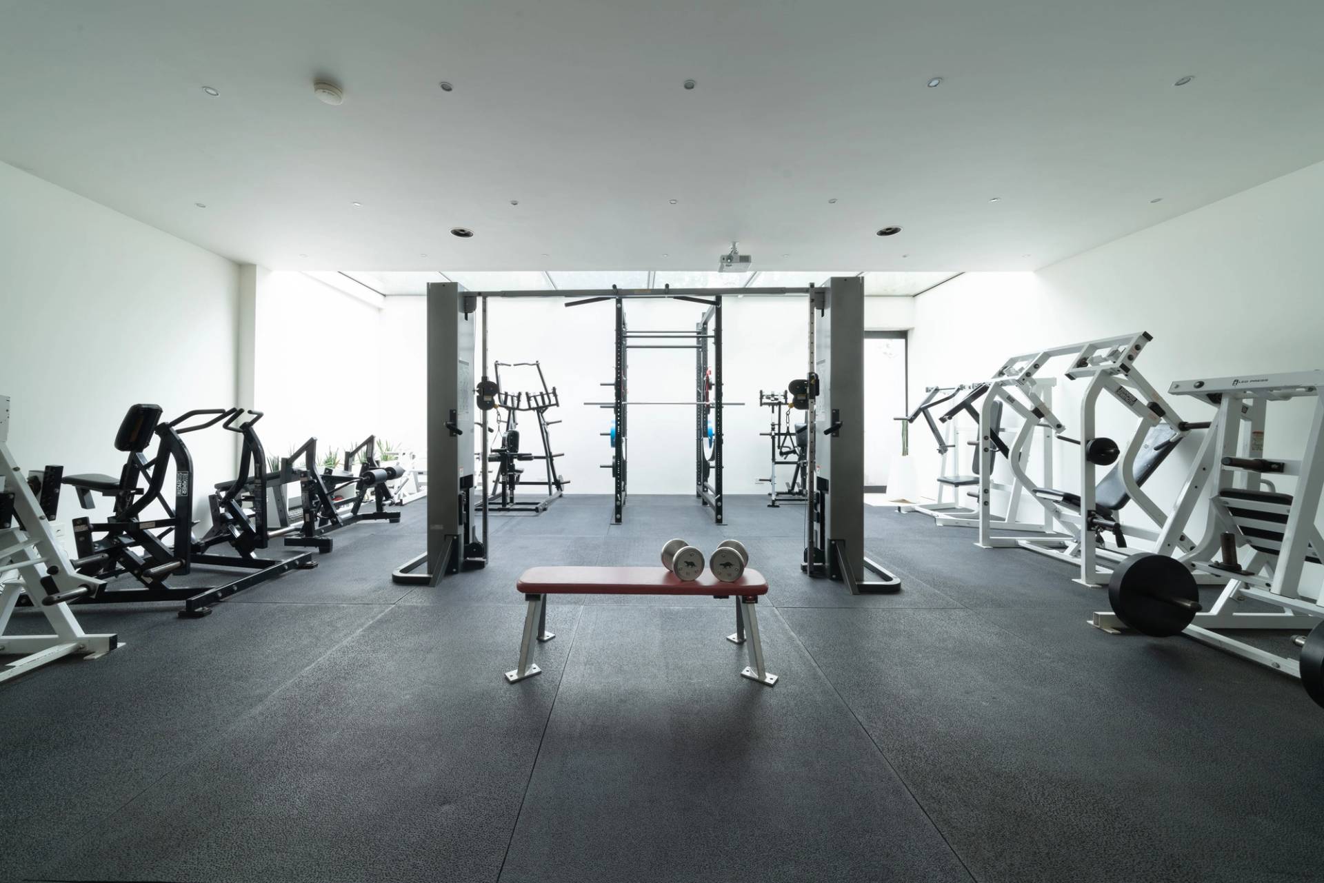 Private subterranean home gym facility with commercial workout equipment, bench press, and black rubber flooring, Love Locations SW6.
