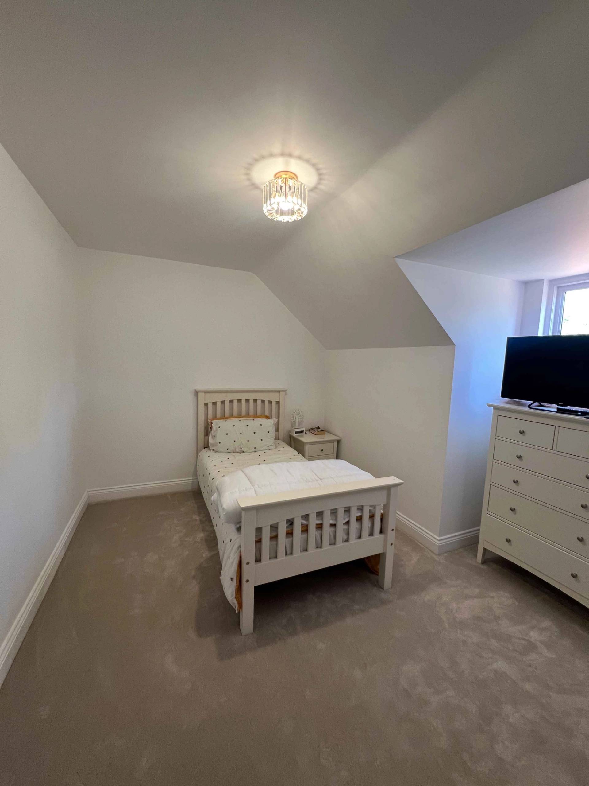 Attic guest bedroom featuring sloped ceilings, white bed, and chest of drawers, Love Locations BR7.
