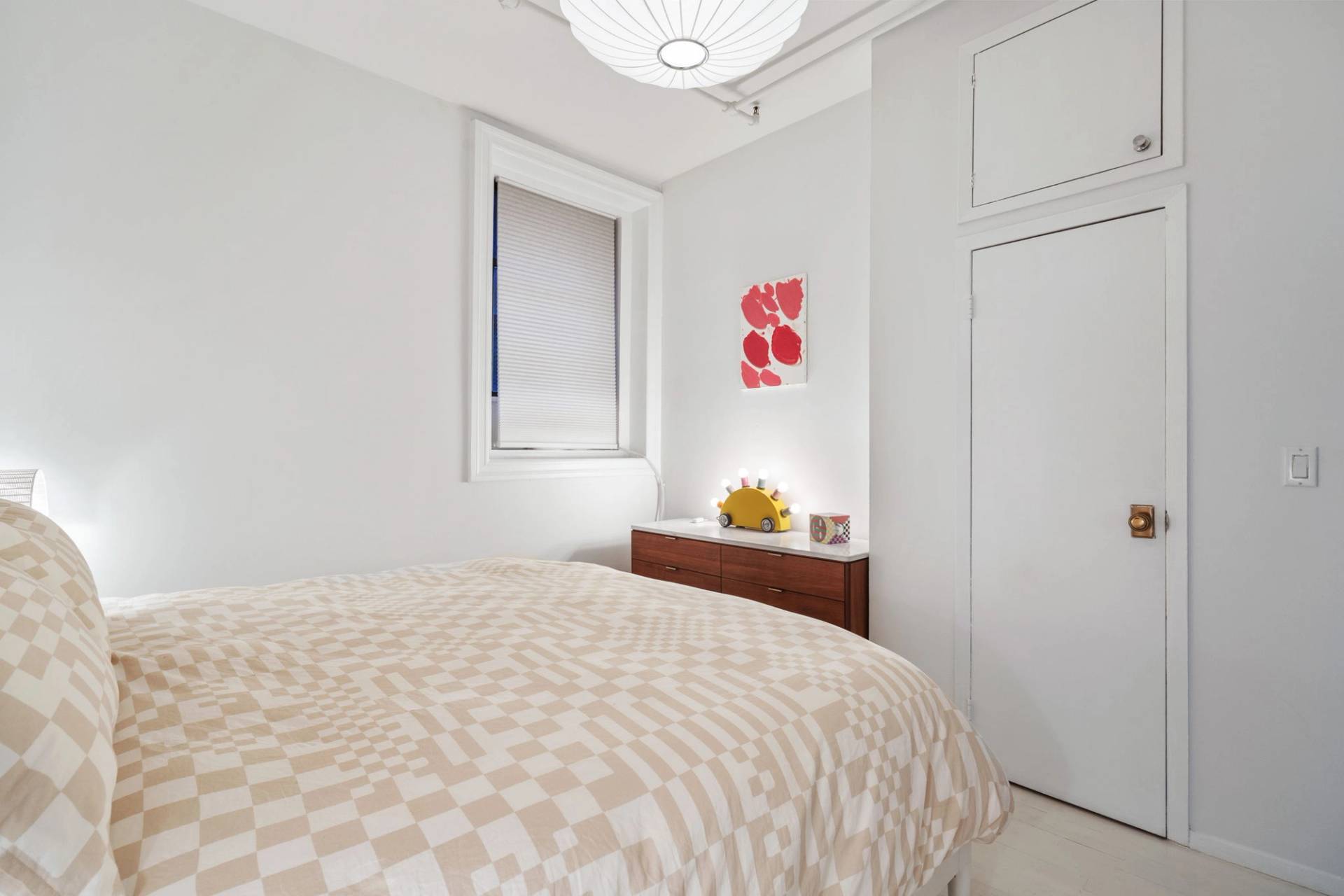 Bright secondary bedroom nook with a wooden dresser and white walls in a Tribeca NY 10007 location house through Love Locations.
