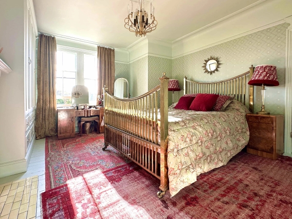 Spacious master bedroom location with brass bed frame, red patterned rug, and chandelier lighting, Love Locations N13.