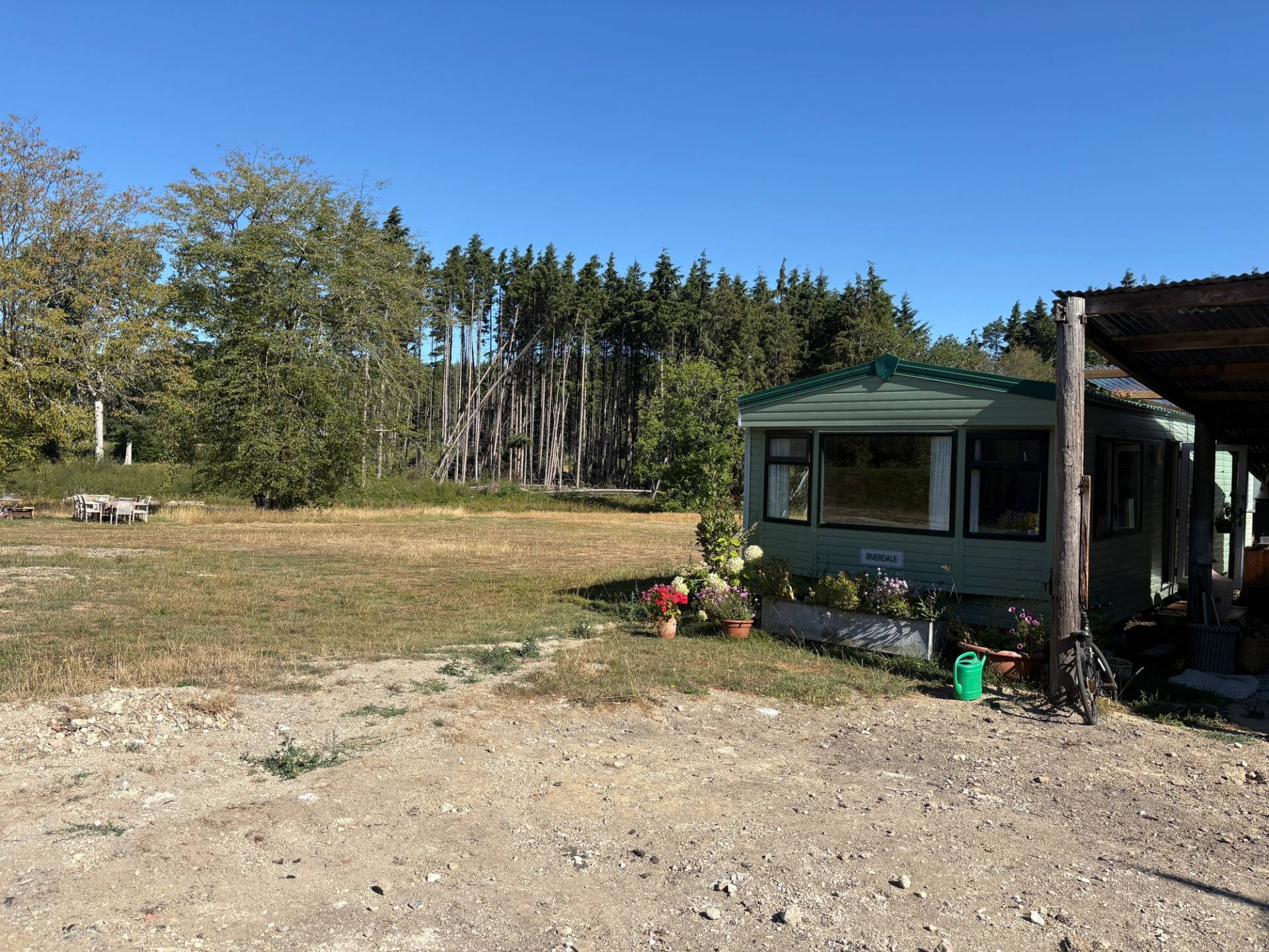 Static green caravan cabin set on gravel ground beside pine tree woods, Love Locations BN8.