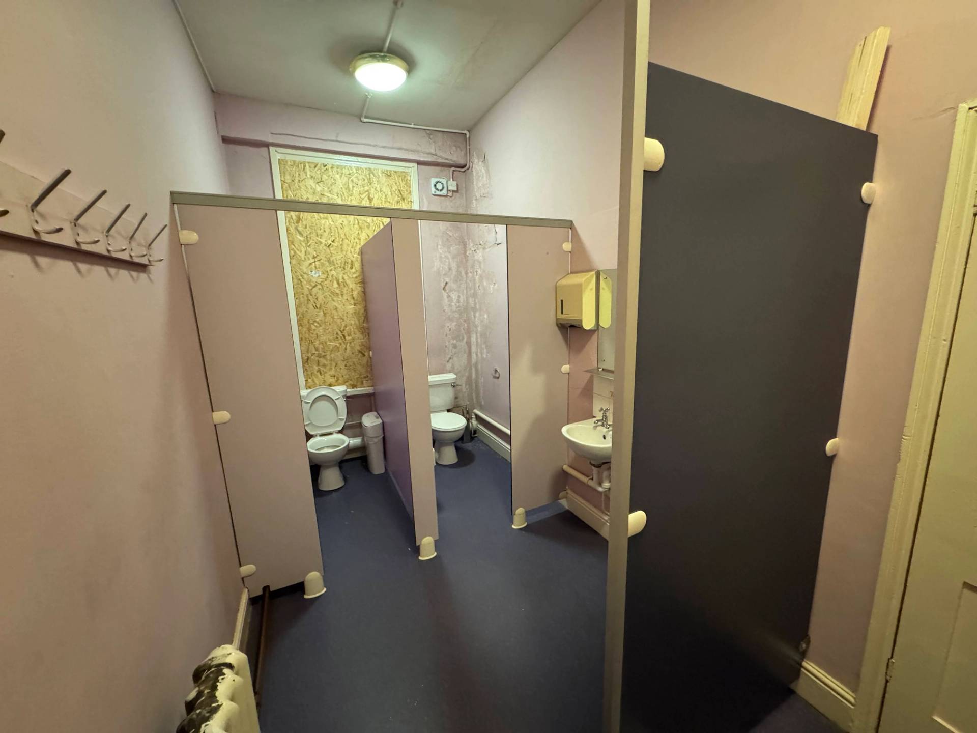 Run-down cloakroom area featuring rows of distressed timber partition screens and coat hooks, Love Locations.