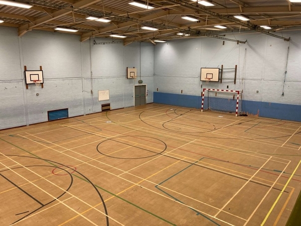 Love Locations indoor sports hall film location CM1: Sprawling school gymnasium floor with basketball hoops, indoor football goals, and multi-sport court lines, ideal for high-energy sports commercials.