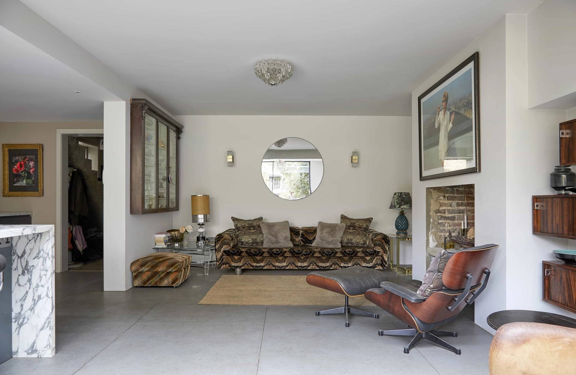 Open-plan living space featuring a long tiger-print sofa, round wall mirror, and Eames recliner, Love Locations N16.