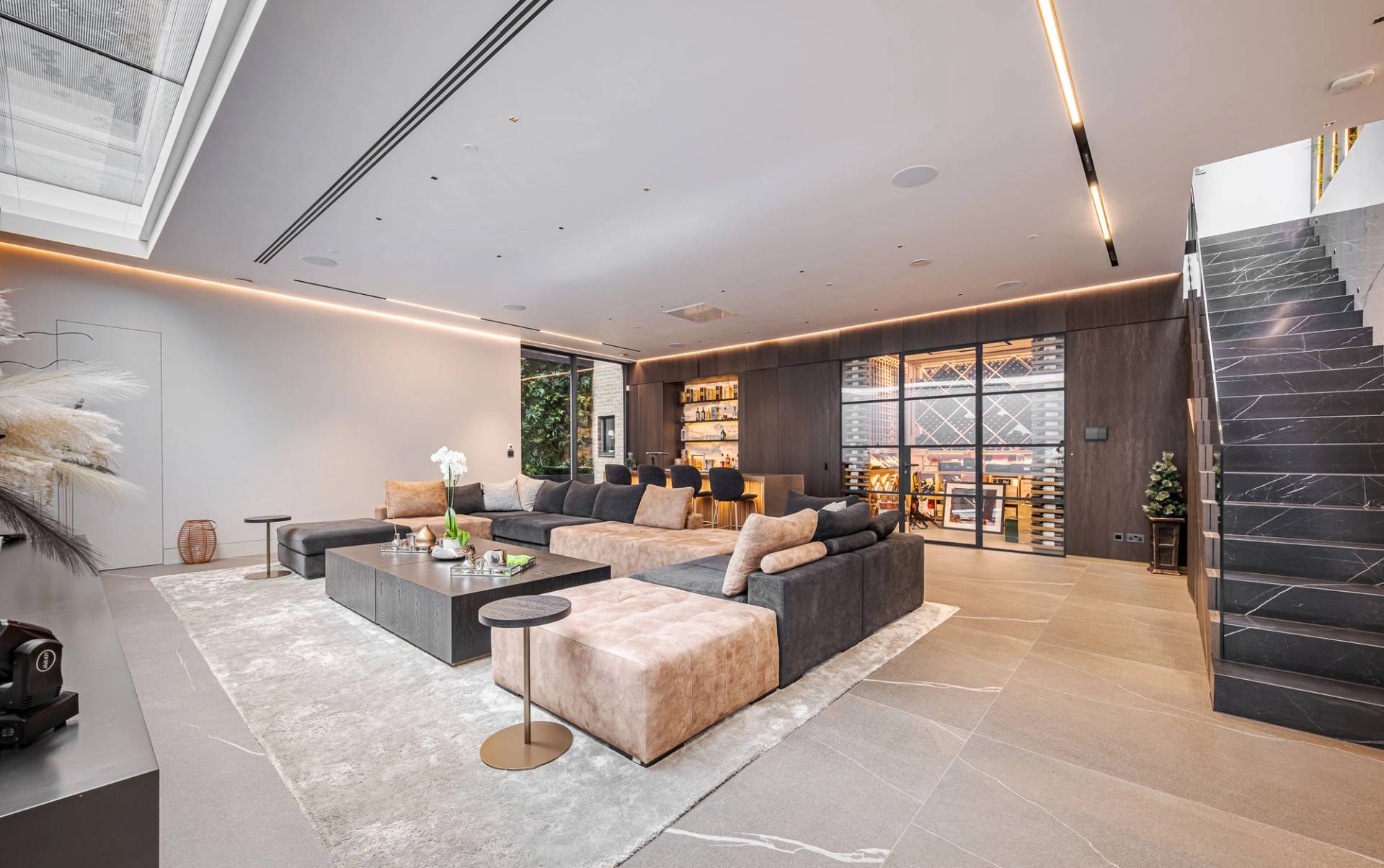 Basement cinema lounge room with beige velvet corner sofa, dark coffee tables, and glass partition doors, Love Locations SW11.