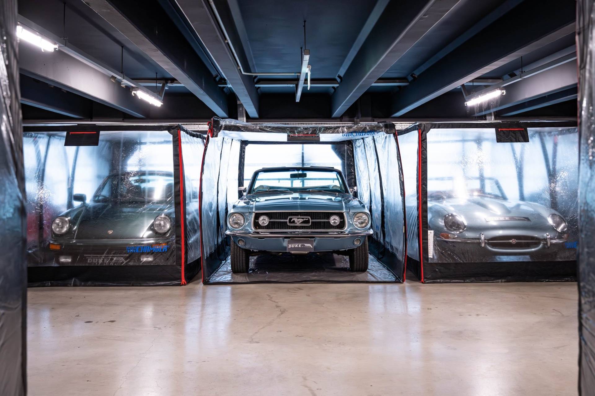 Classic blue Ford Mustang flanked by vintage sports cars in protective capsules in Brentford TW8 by Love Locations.