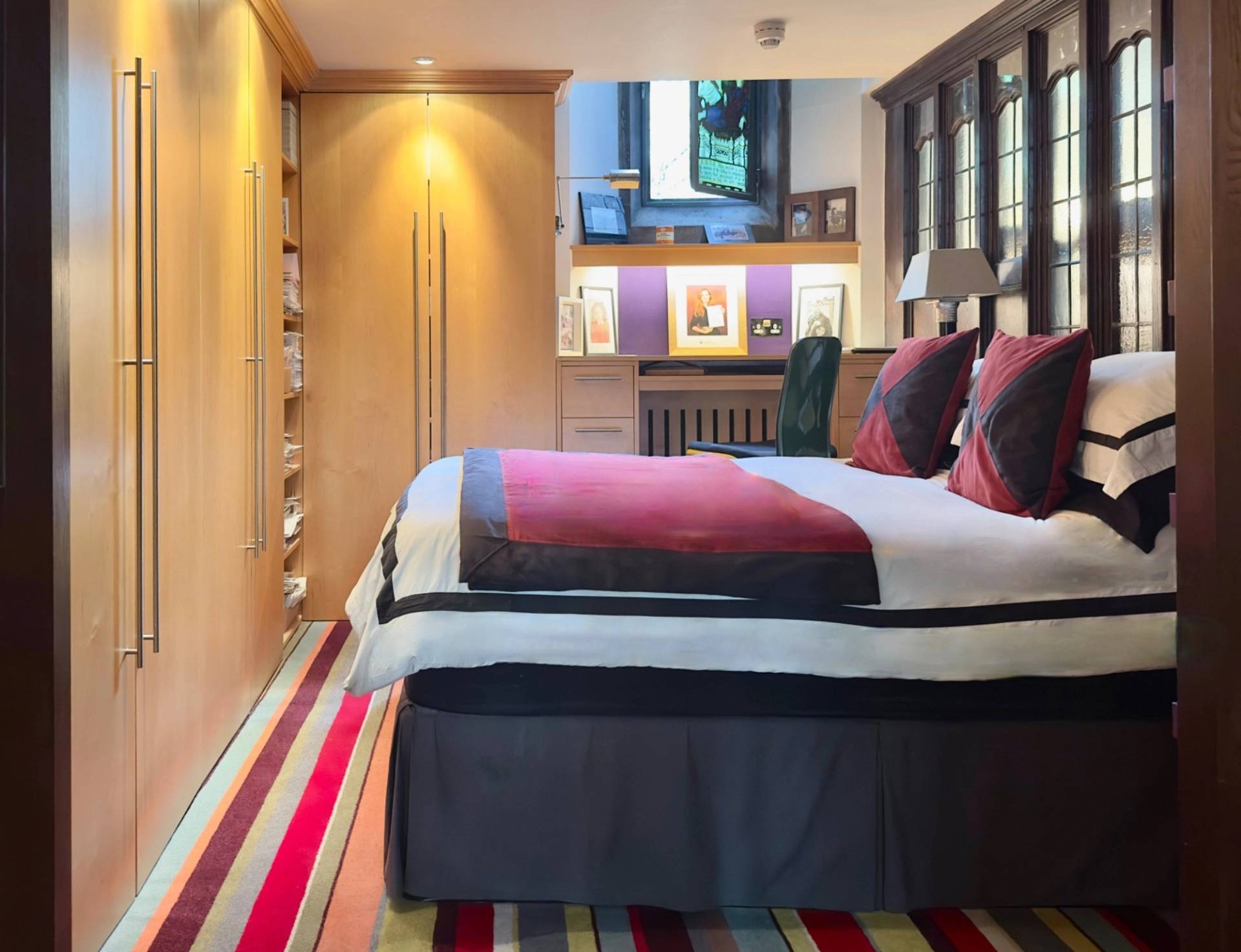 Boutique bedroom with vibrant red and dark blue accents and built-in wooden wardrobes in an Oval SE5 location house via Love Locations.