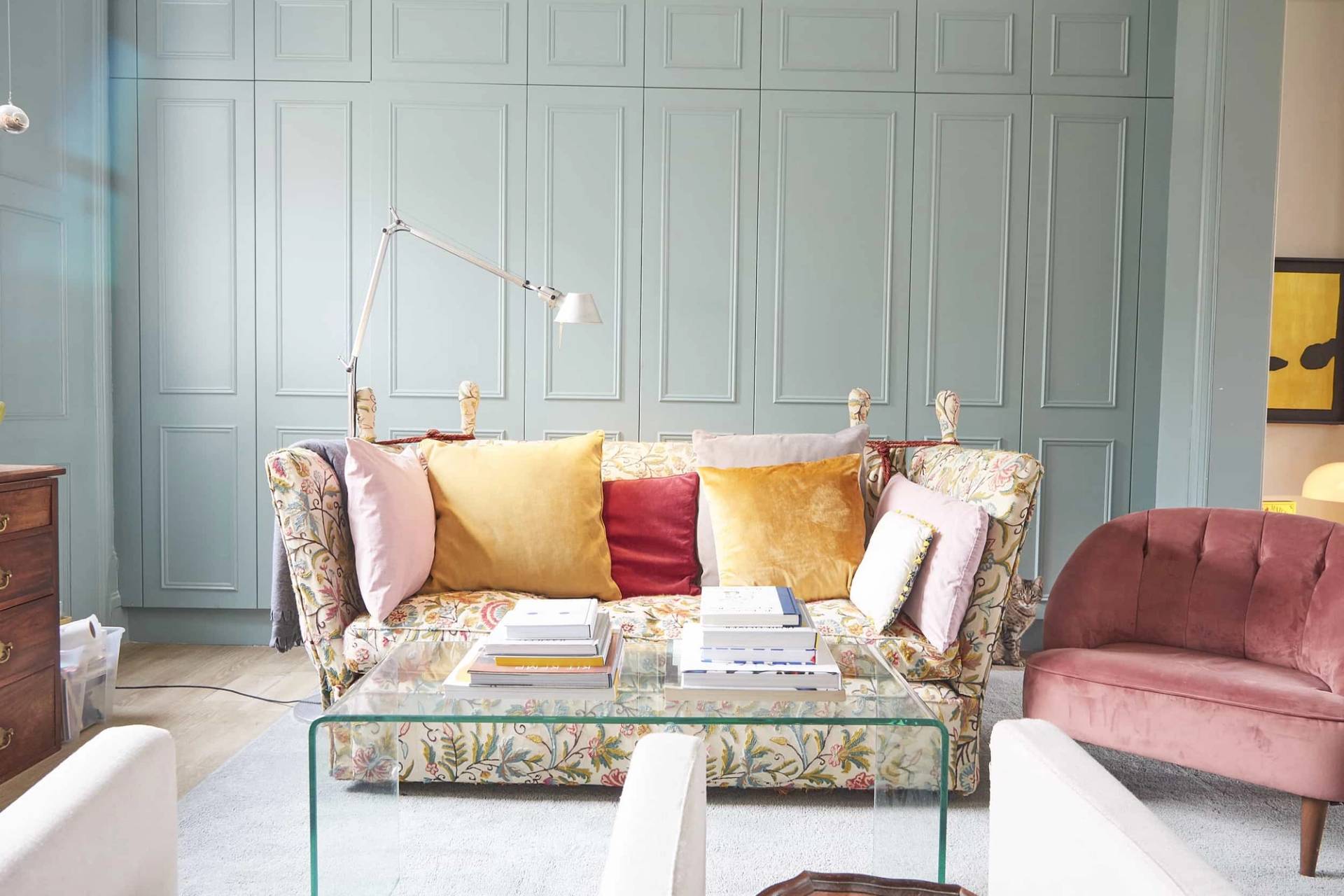 Cozy sitting corner set against duck-egg blue panelled walls with a floral upholstered sofa and velvet throw cushions, Love Locations N5.