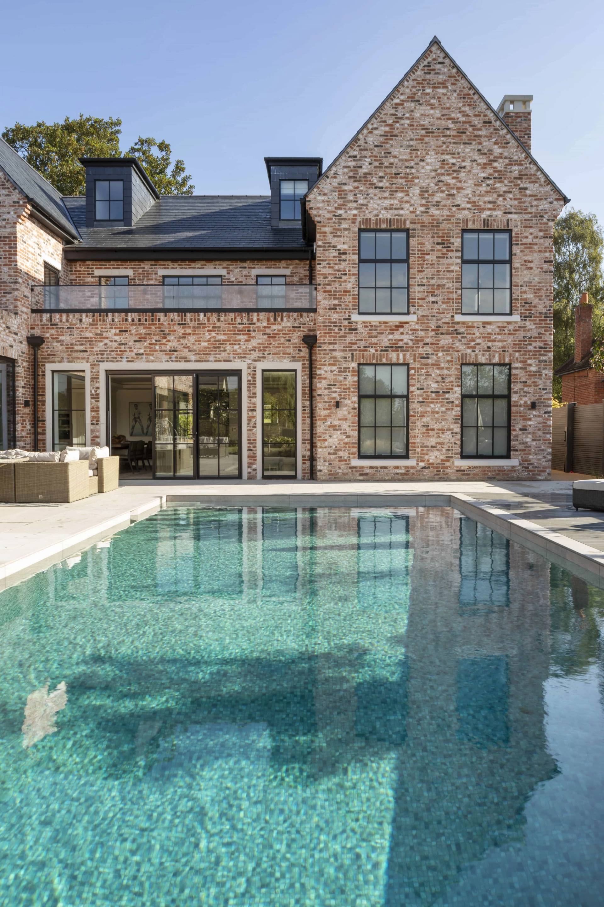 Symmetrical shot of a heated outdoor swimming pool set against a grand brick country house, Love Locations HP18.