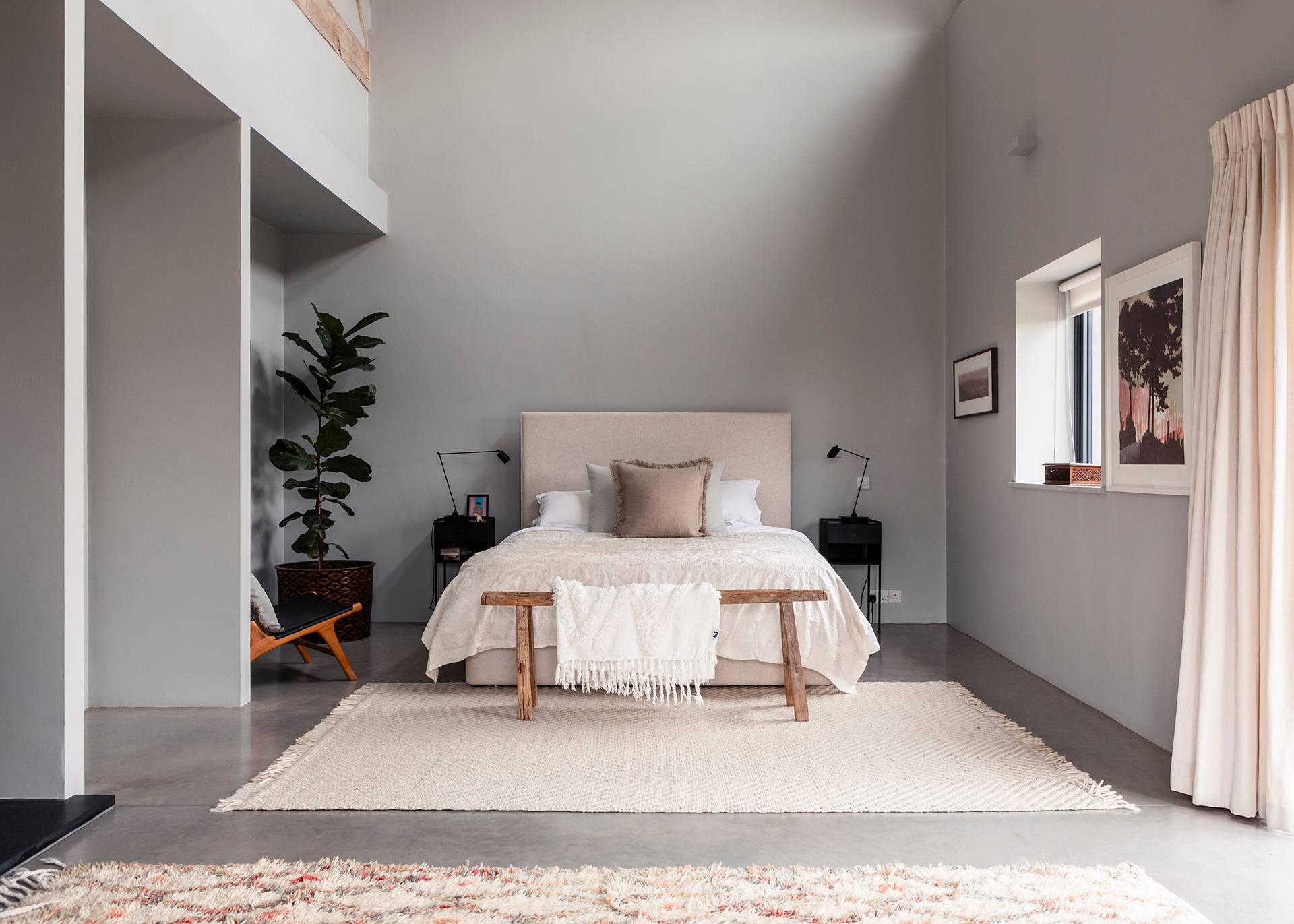 High-ceiling master bedroom suite with neutral linens, large potted fiddle-leaf fig, and polished concrete flooring, Love Locations SN8.