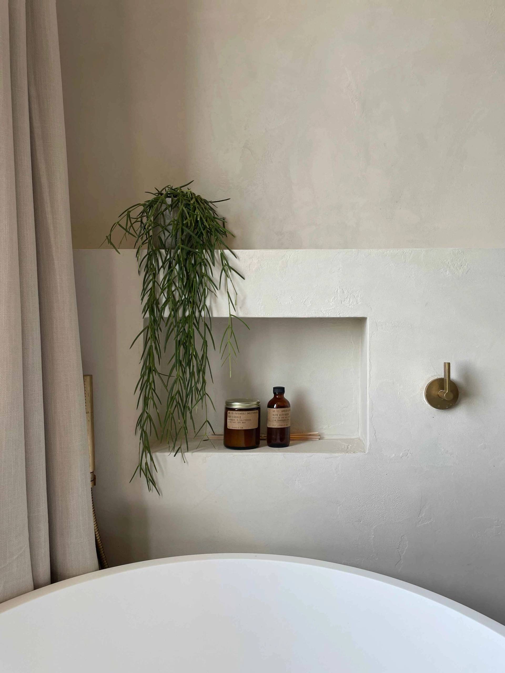 Minimalist plaster bathroom alcove shelf detail with trailing greenery and brass fixtures, Love Locations.