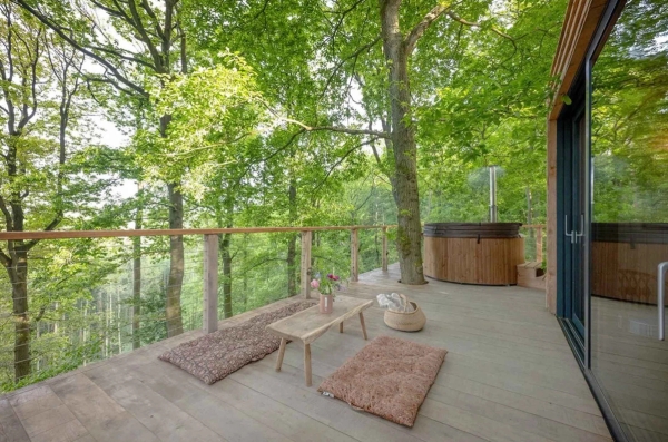 Outdoor wooden treehouse balcony deck equipped with floor cushions, a low coffee table, and an integrated hot tub, ideal for luxury glamping campaigns, Love Locations.