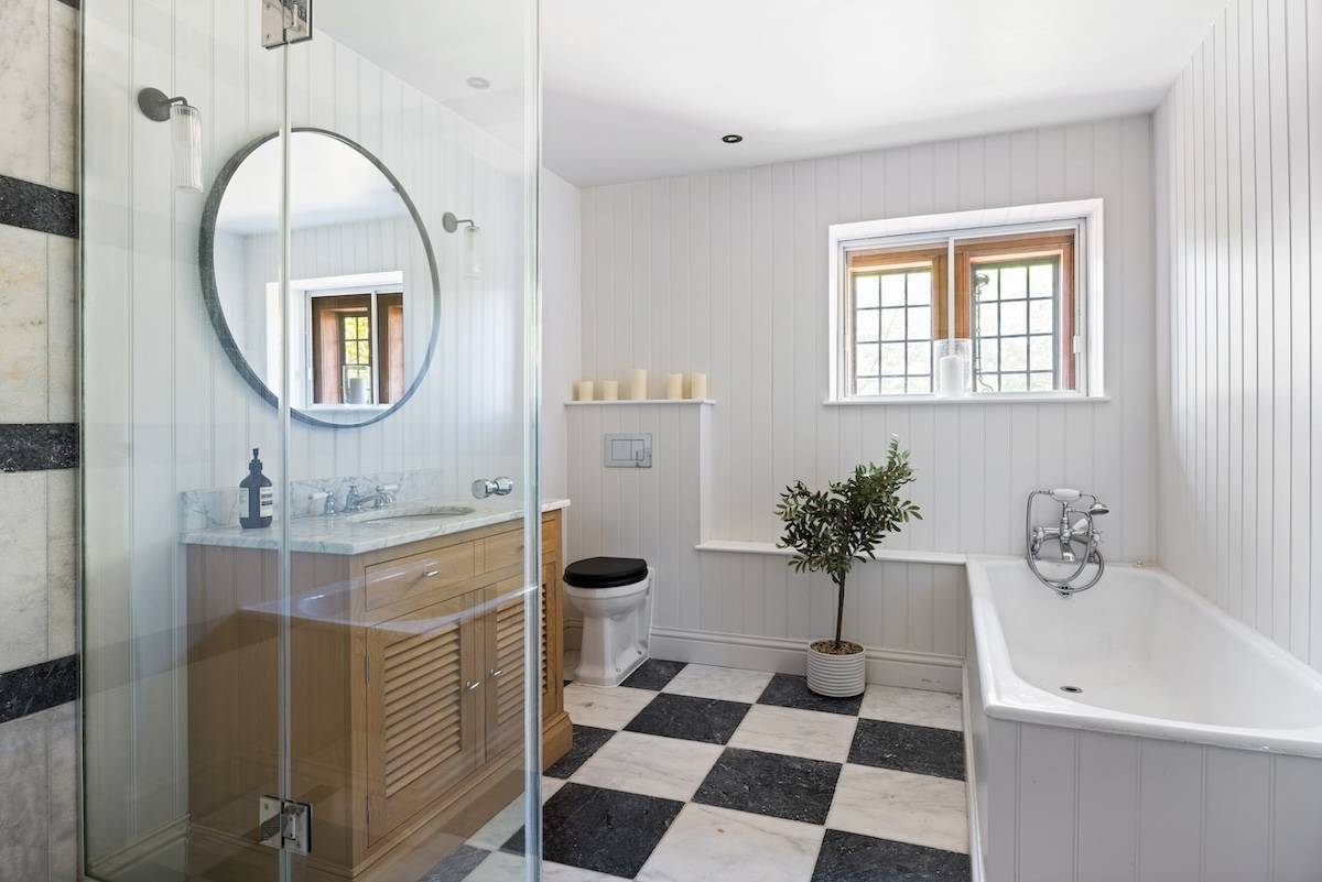 Modern bathroom with black and white checkerboard tile floor, glass shower enclosure, and circular mirror, Love Locations RH13.
