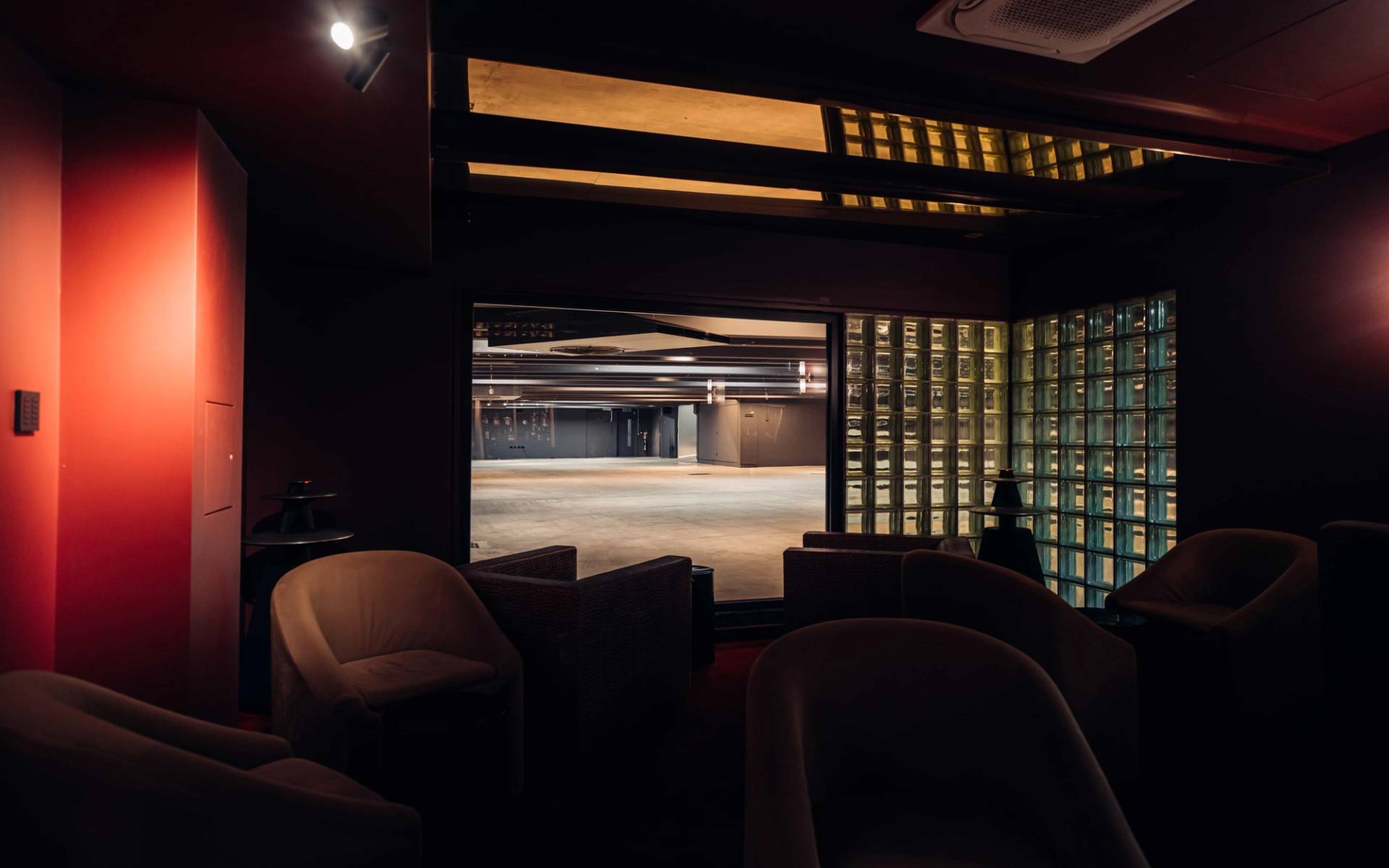 Low-lit cocktail bar lounge filming space in Brentford TW8 by Love Locations, with plush velvet Tub chairs and view into a supercar showroom.
